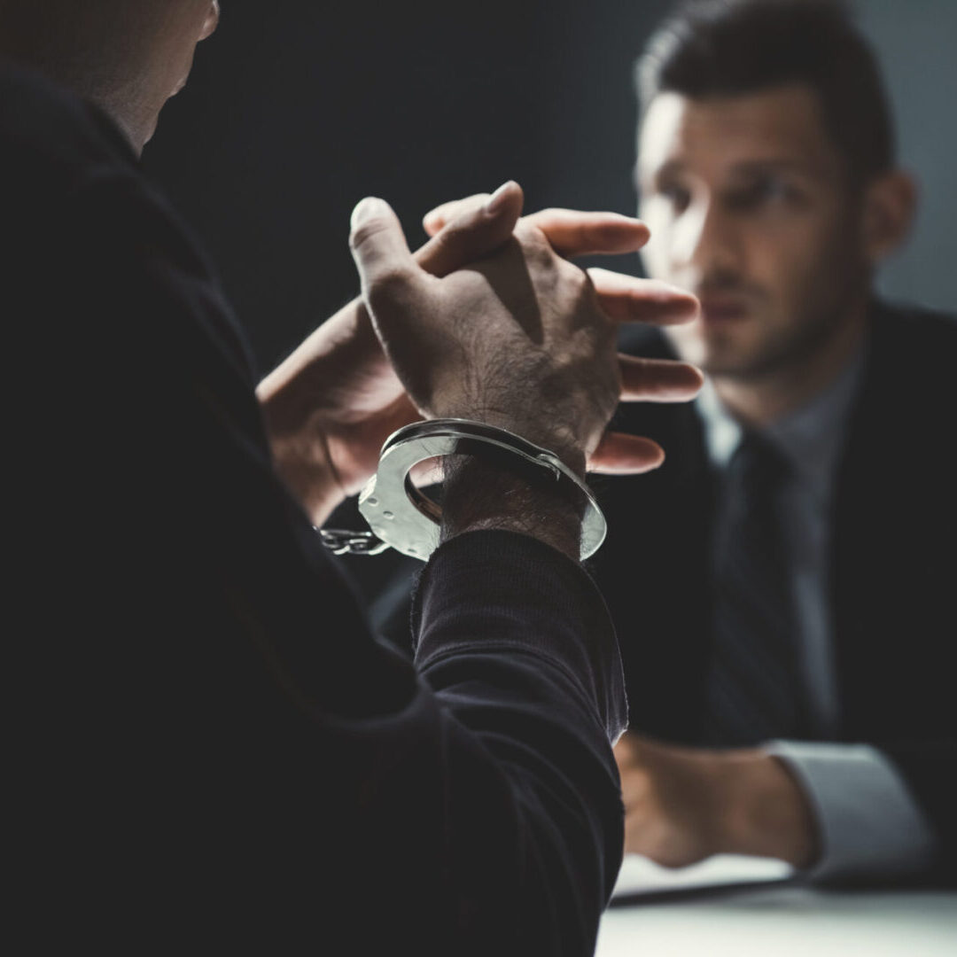 Criminal man with handcuffs being interviewed in interrogation room after committed a crime